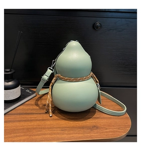 Detail view of a light green gourd-shaped leather bag with a woven strap on a wooden desk