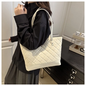 Macro detail of beige quilted tote bag with metallic bow charm and refined stitching