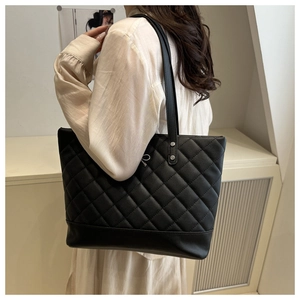 Detail of a large black quilted tote bag with silver metal hardware worn on the shoulder