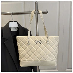 Detail of cream quilted tote bag featuring silver bow hardware and elegant stitching