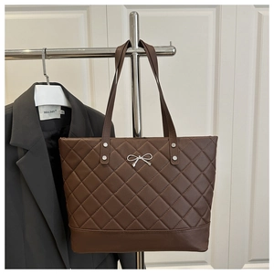Close-up of brown quilted tote bag with silver bow charm on a clothing rack