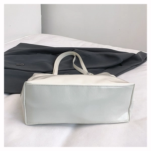 Detail view of the flat rectangular base and neat stitching on a white soft leather tote bag