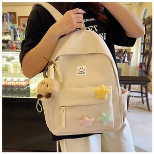 Close-up of a cream-colored canvas backpack with a smile logo and plush star charms