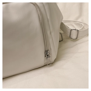 Close-up of metal zipper detail and adjustable strap on white faux leather tote bag