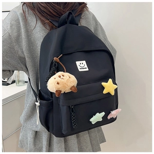 Detail of black nylon backpack featuring cute plush star charms and a rubber smiley badge