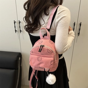 Pink corduroy mini backpack with black smiley face and white pompom charm accessory