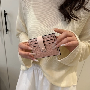 Pink woven card holder with button closure and card slots held in a lifestyle setting