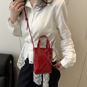 Minimalist red glossy leather tote bag with unique knot handles and a shoulder strap