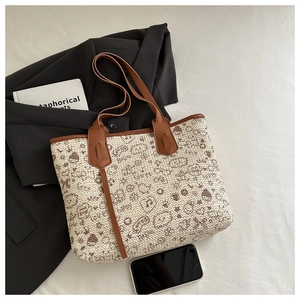 Flat lay of tote bag with cartoon patterns, brown leather trim, and commute styling props