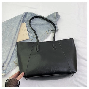 Close-up of black leather tote bag on white cloth with denim jacket and book