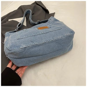 Gros plan du sac cabas en denim bleu clair avec bords effilochés et écusson en cuir brun