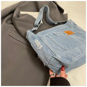 Détail du sac à bandoulière en jean bleu clair avec bords effilochés et écusson en cuir