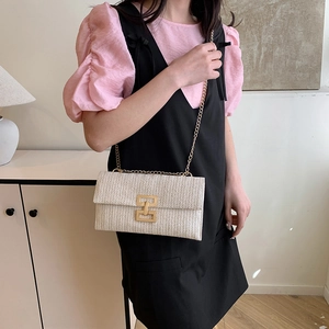 Sac bandoulière tressé blanc avec chaîne dorée et fermoir porté par un mannequin