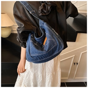 Detail of vintage denim crossbody bag featuring white stitching and brown leather label