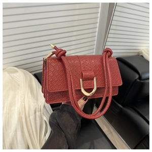 Detail of red croc-embossed shoulder bag featuring a gold horseshoe buckle and knotted strap