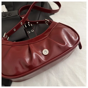 Detail of burgundy glossy leather underarm bag with pleated texture and silver buckle