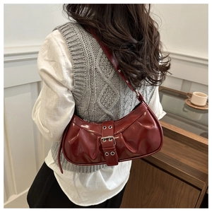 Detail of dark red saddle bag with pleated design and metallic buckle on wooden background