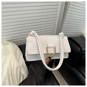 Detailed view of white faux-crocodile shoulder bag with gold U-shaped buckle and woven strap