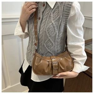 Detailed view of a brown glossy patent leather crescent shoulder bag with pleated texture