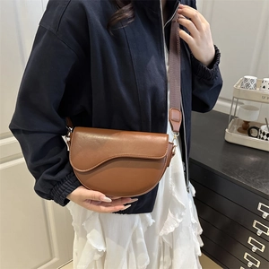 Brown leather saddle shoulder bag with wide textile strap worn by model in casual setting