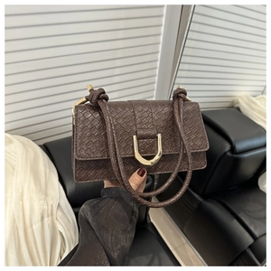 Detail of dark brown crocodile texture bag with gold horseshoe buckle and braided straps