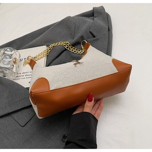 Dettaglio borsa a spalla in tela beige con finiture in pelle marrone e ciondolo a cervo