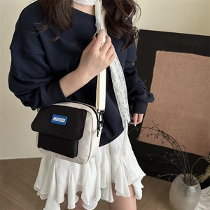 Borsa a tracolla quadrata minimalista crema e nera con ampia tracolla indossata da una modella