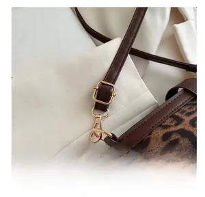 Détail macro du crochet doré et de la bandoulière en cuir marron sur le sac léopard
