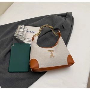 Mini borsa in tela e pelle con ciondolo cervo dorato accanto a un tablet per scala