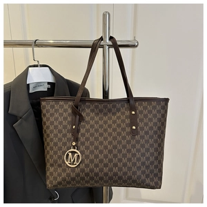 Gros plan d'un sac cabas marron à monogramme M avec pendentif doré circulaire