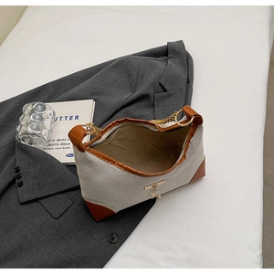 Dettaglio della borsa tote in tela con finiture in pelle marrone e catena su blazer grigio