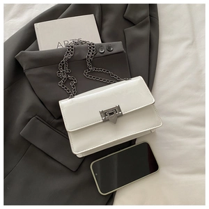 Detailed close-up of white patent leather chain bag with geometric buckle and grey blazer