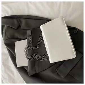Detailed view of white patent leather crossbody bag with black metal chain strap and sleek finish