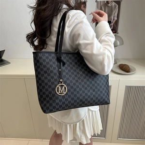 Sac cabas chic à motif M gris avec pendentif doré dans un décor intérieur épuré