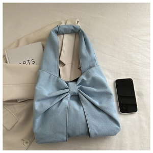 Vista piatta della borsa tote in denim azzurro con grande fiocco su sfondo di stoffa