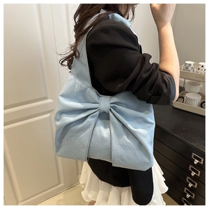 Dettaglio borsa a spalla in denim azzurro con grande fiocco indossata da modella