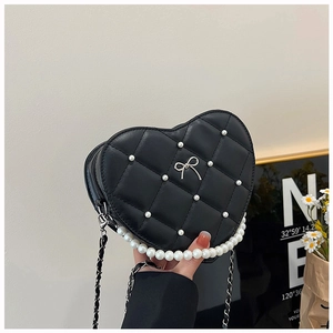 Detail of heart-shaped quilted leather bag with pearl handle and metal bow accent