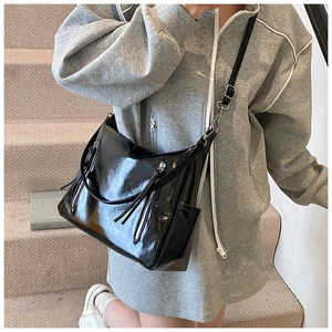 Détail du sac hobo en cuir verni noir avec pompons et ferrures argentées porté par un mannequin