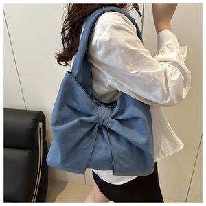 Detail shot of a blue denim tote bag featuring a large bow on a model in a modern room