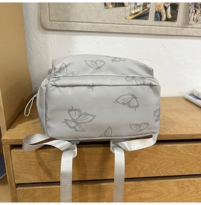 Detail of silver-grey backpack showing satin-finish nylon texture and butterfly patterns