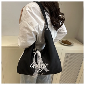 Rear view of model wearing a black nylon tote bag with lace detail and white lettering