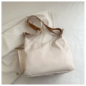 Detail view of cream nylon shoulder bag with wide brown strap on textured fabric