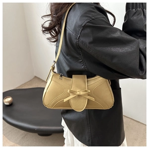 Détail du sac à bandoulière jaune moutarde avec nœud porté par un mannequin en intérieur
