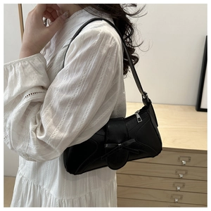Vue latérale d'un sac à bandoulière noir avec nœud porté avec une robe blanche chic