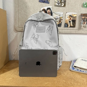 Gray butterfly pattern backpack with front leather label shown next to an iPad for size reference