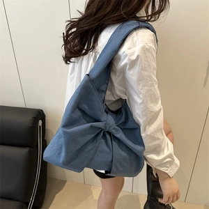 Borsa a spalla in denim blu con grande fiocco mostrata su modella di profilo
