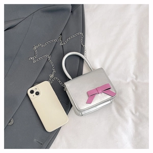 Mini silver handbag with pink bow and chain shown next to smartphone for scale
