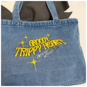 Close-up of yellow embroidery on blue denim tote bag with Groovy Trippy Heart design