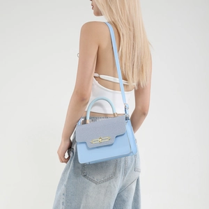 Light blue leather and denim crossbody bag with gold handle shown from a side-rear view