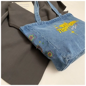 Detail of blue denim tote bag with Trippy Heart embroidery on grey suit background